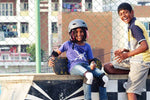 Two kids smile while sitting in a skatepark.